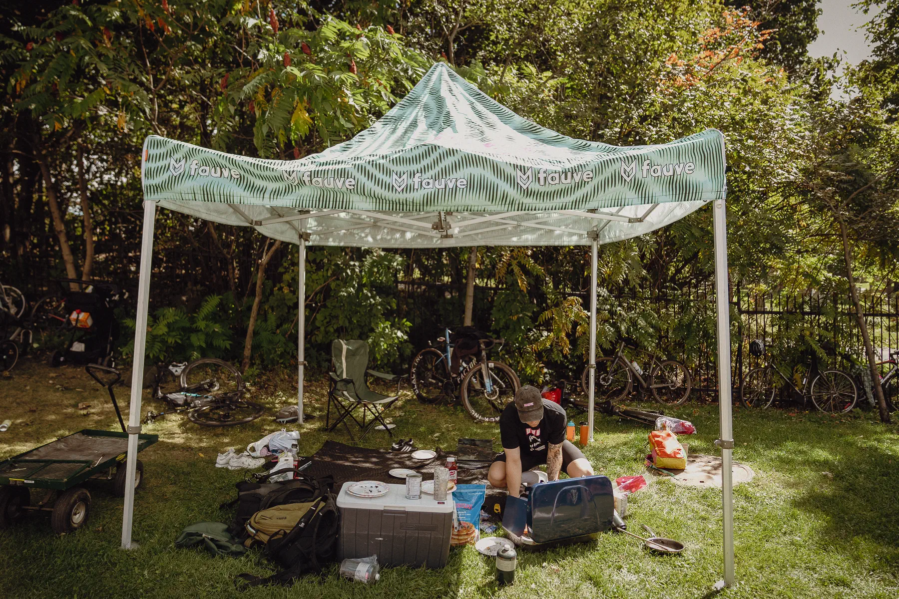 A small race-week canopy sits beneath the trees with cases, bags and equipment spread across the grass