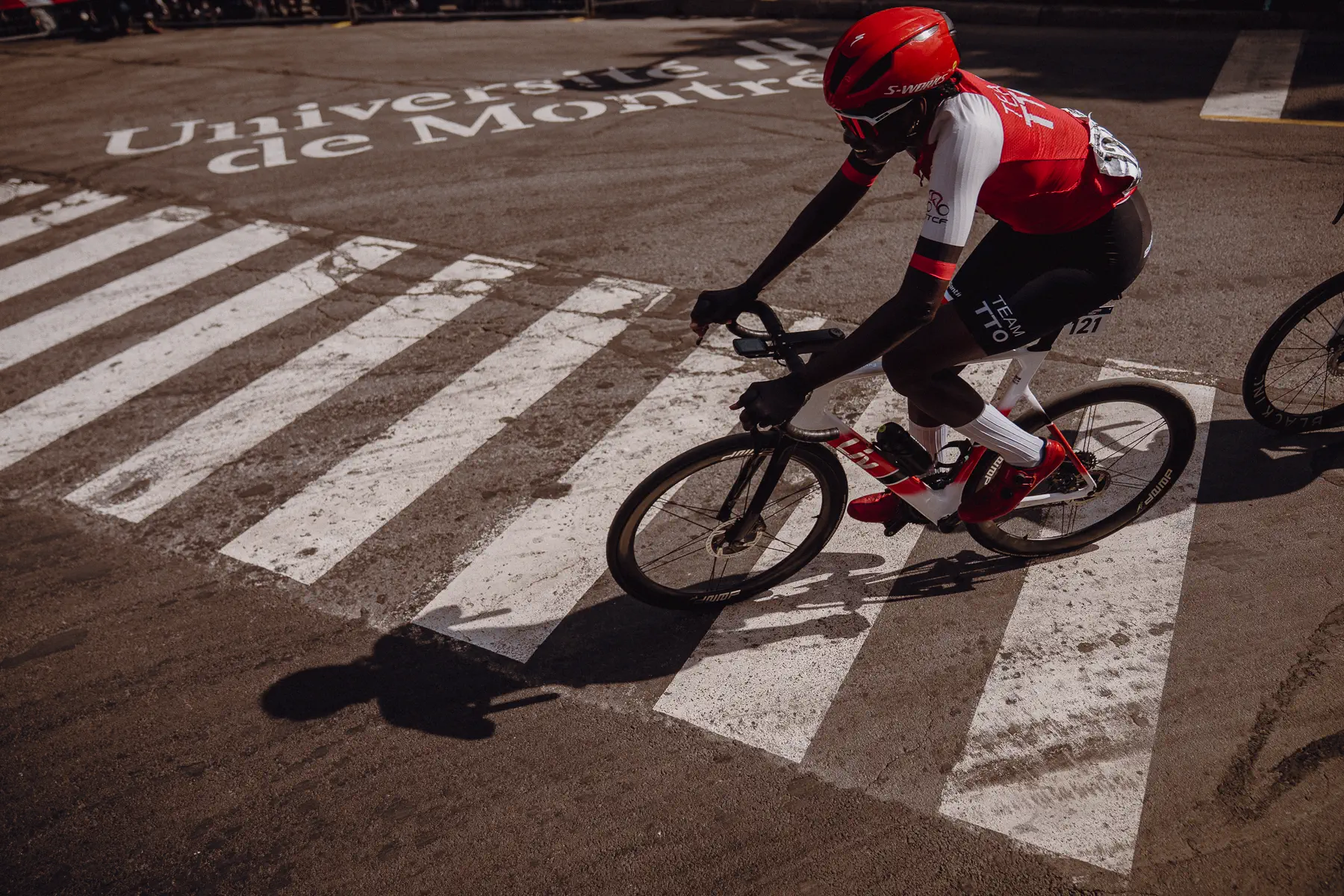 A lone rider cuts across bold road markings in a graphic overhead race-day frame