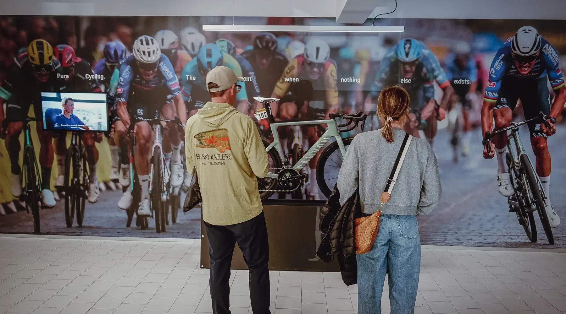Two visitors pause in front of large cycling imagery inside a Montréal event space