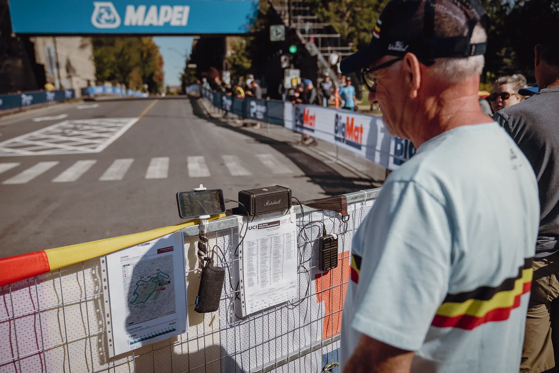 A race staffer studies printed course sheets beside the barriers before the road closes