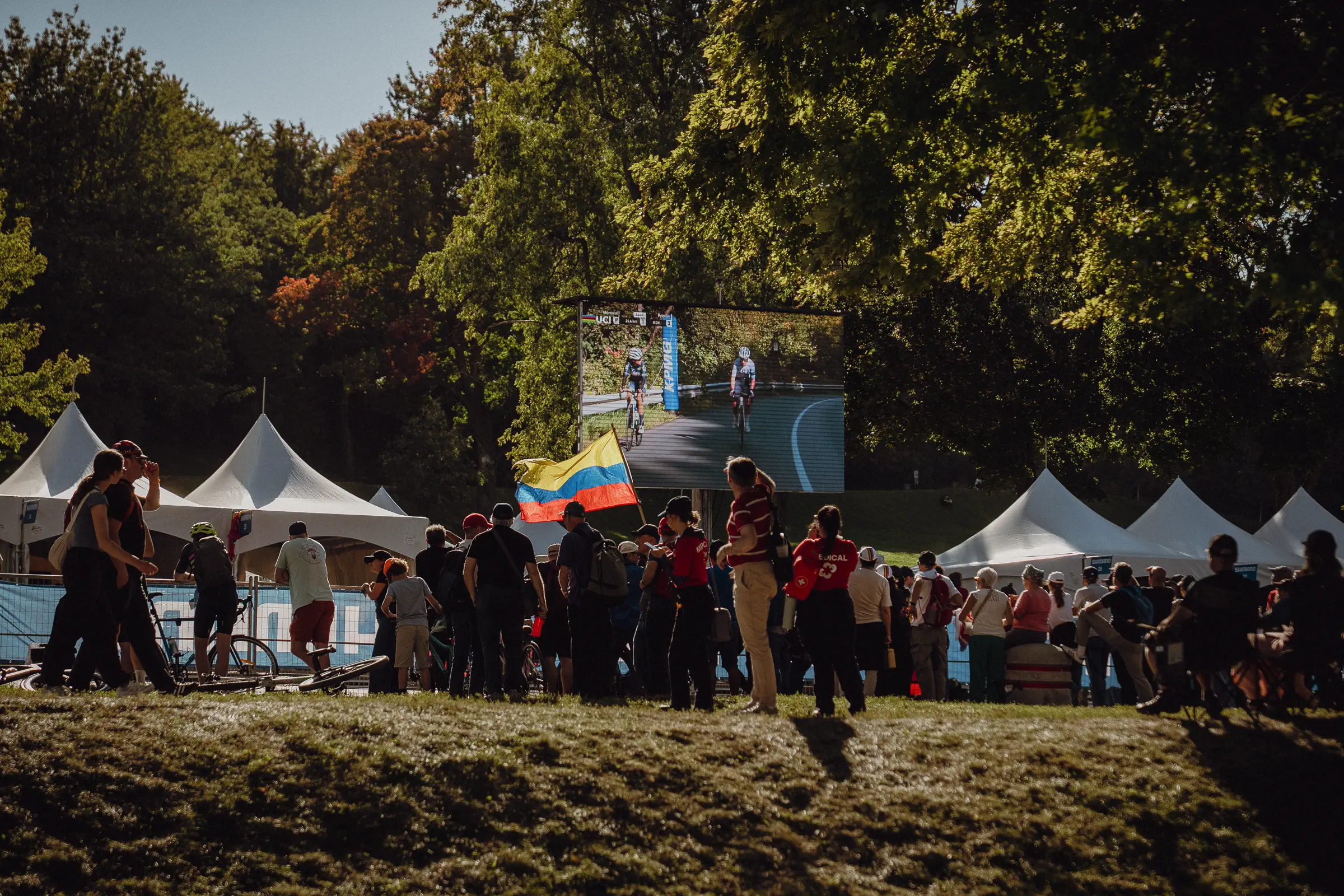 Spectators gather around tents and screens in the shaded Montréal fan zone beneath Mount Royal