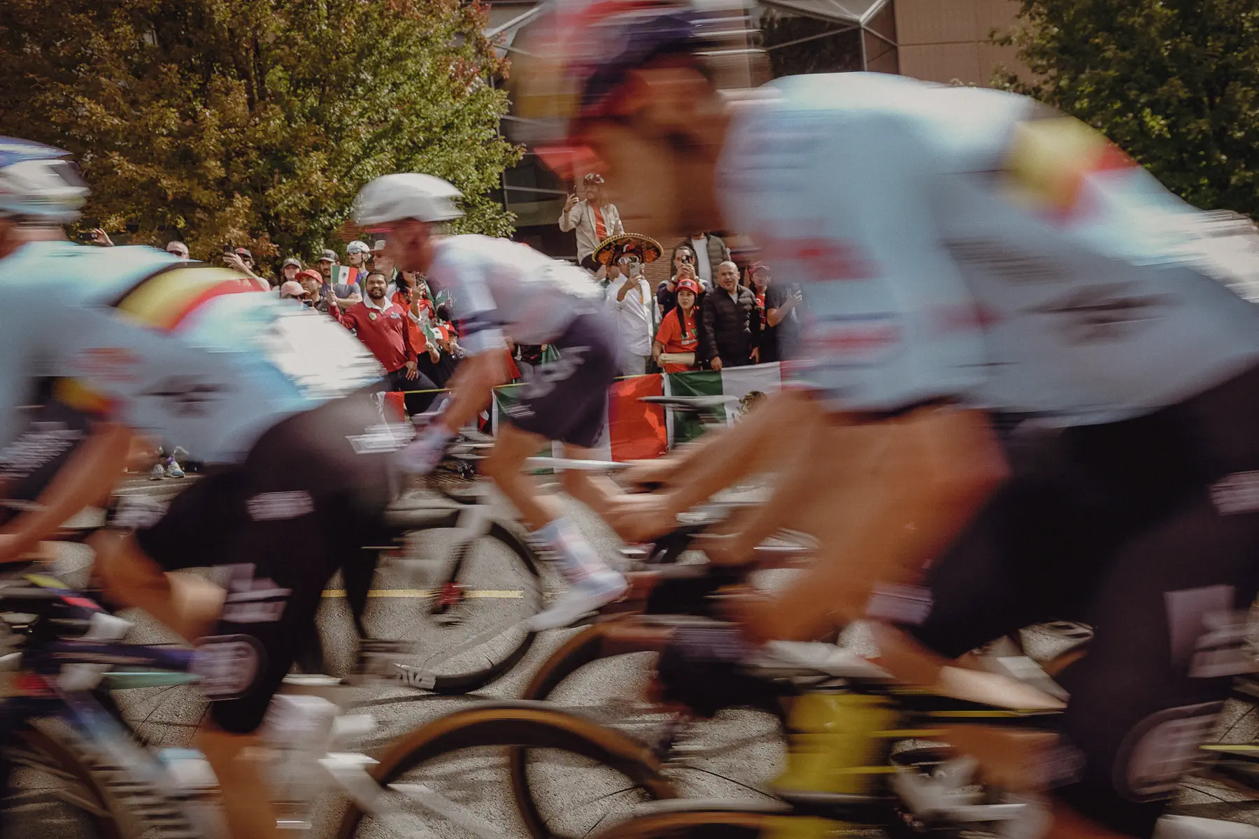 The Elite Men peloton rushes past at close range in a dense blur of national colors and speed