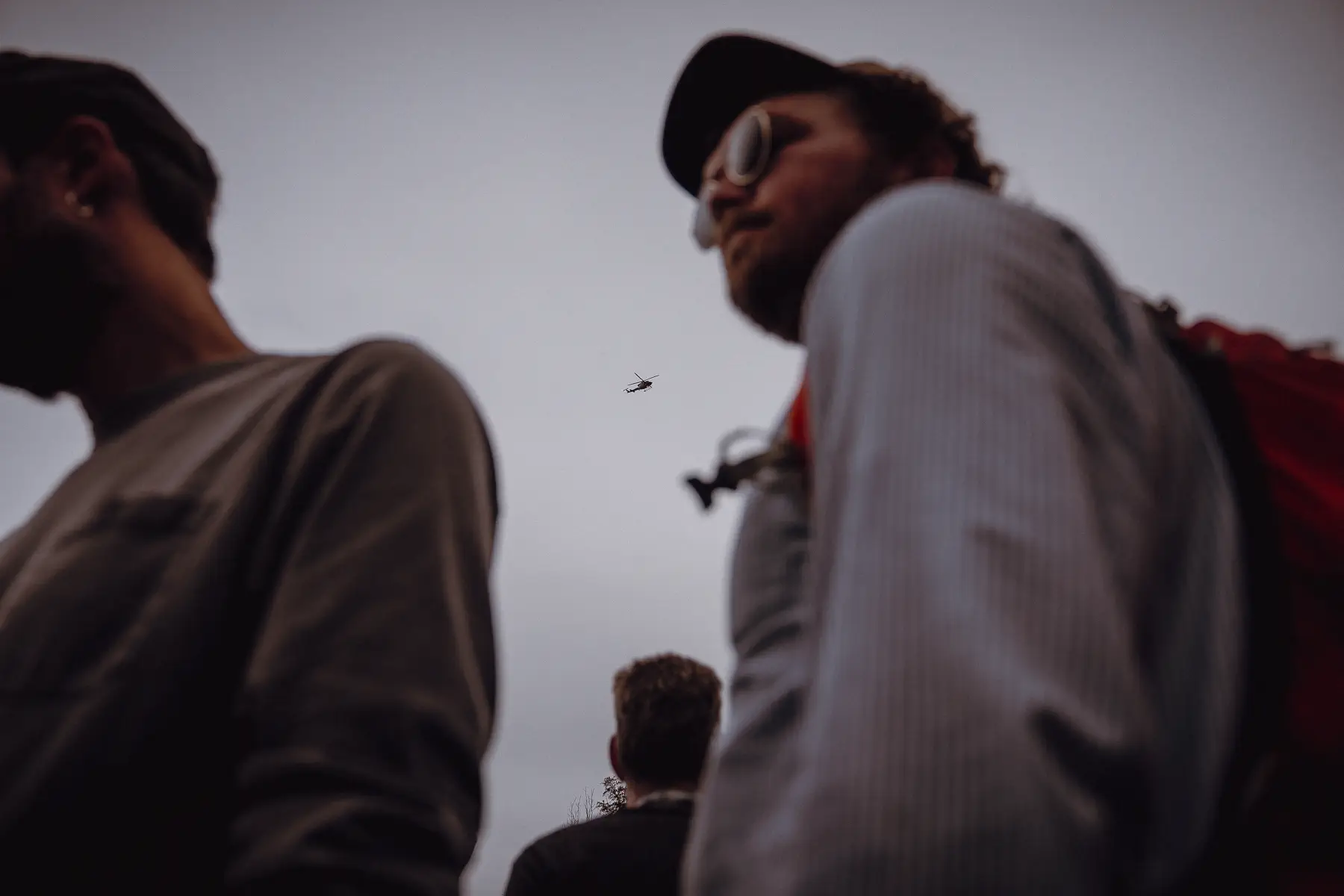 Two spectators stand in deep shadow at the course edge, waiting for the next rush of the race