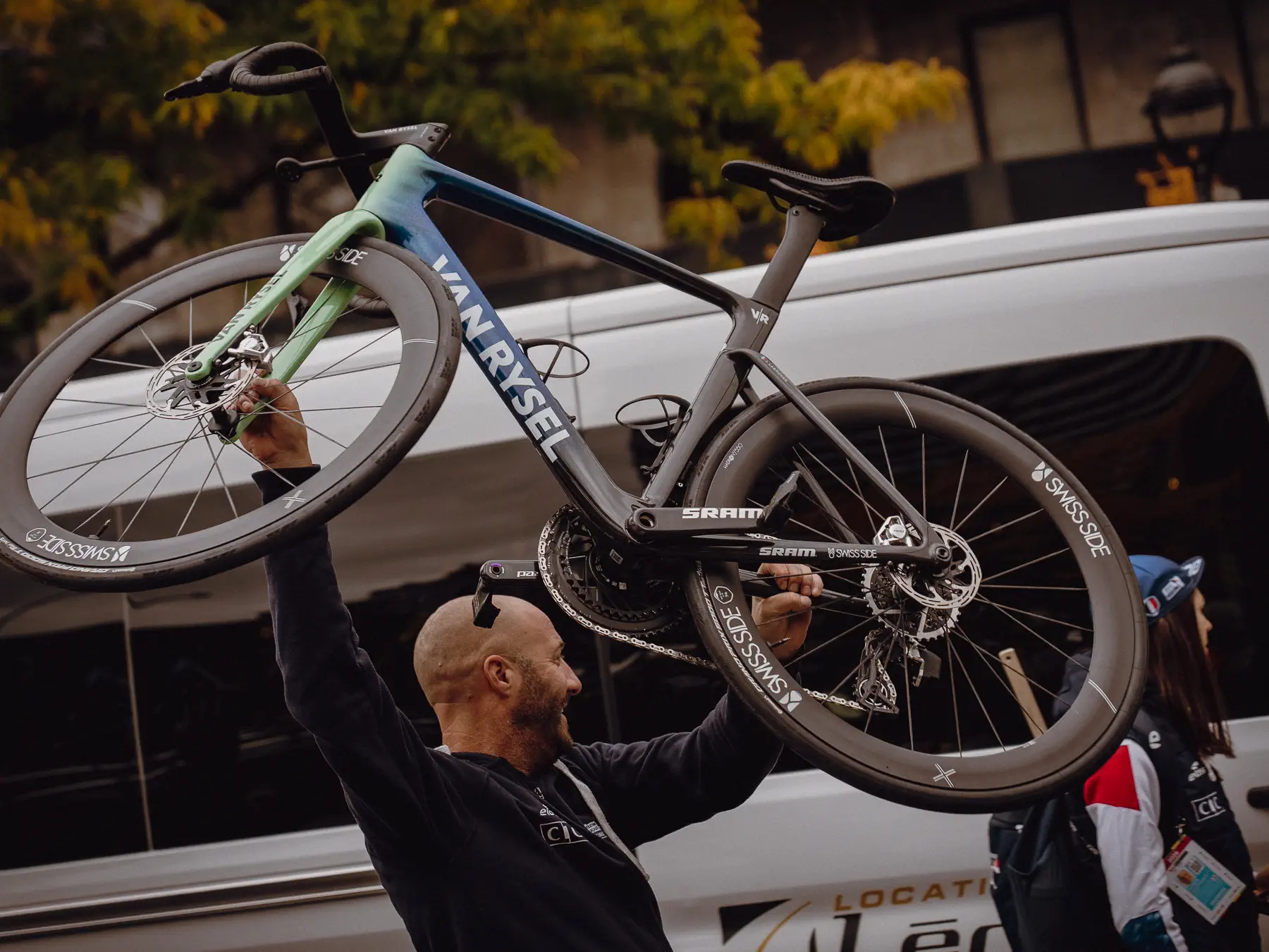 Team staff lift a race bike onto a support vehicle beside the course